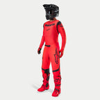 Pilote de motocross portant une tenue de course complète, maillot et pantalon Supertech Ember LE en rouge fluo et noir, casque noir avec lunettes, bottes et gants assortis rouge et noir, tenue professionnelle coordonnée pour la course tout-terrain