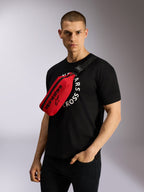 Alpinestars Only Linear heuptas in rood en zwart, cross-body gedragen over een zwart grafisch T-shirt, met opvallende zwarte Alpinestars-logo's en een verstelbare webbing riem voor een casual urban look
