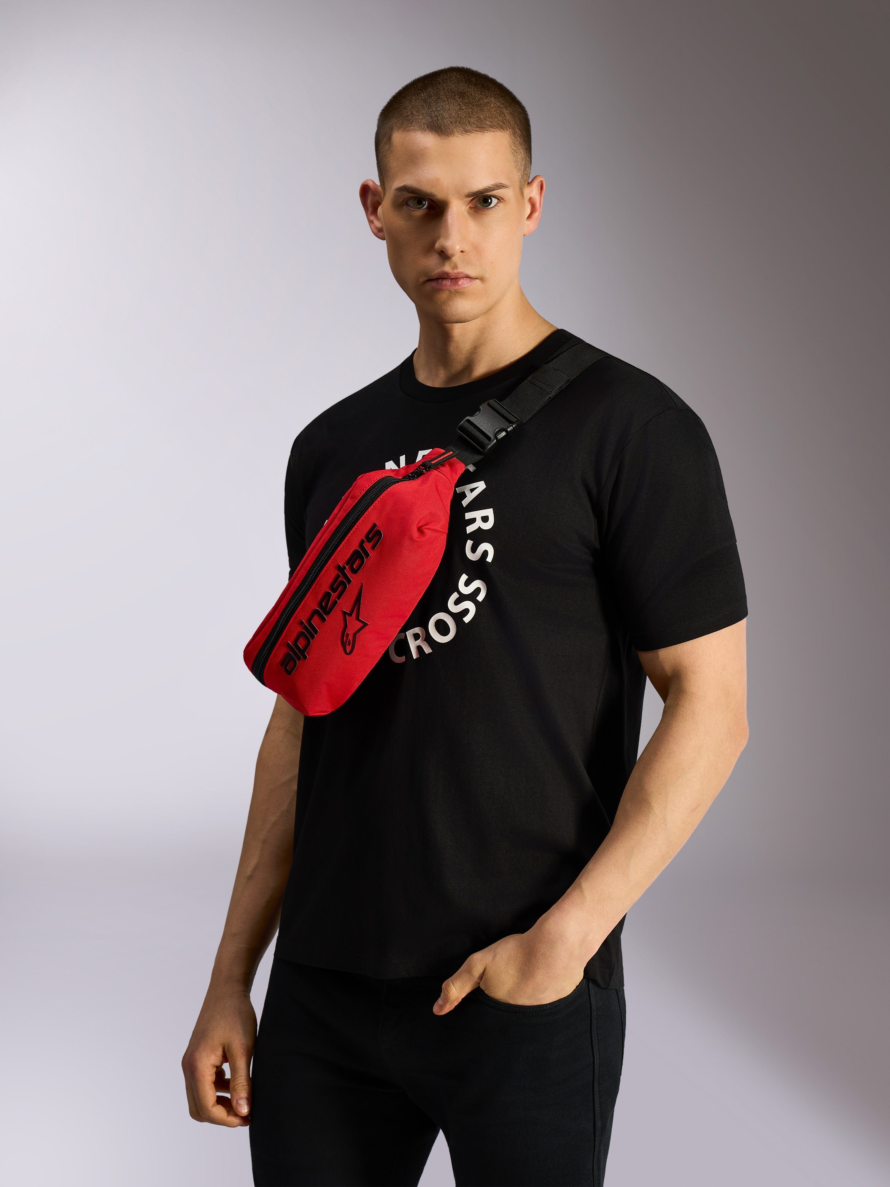 Alpinestars Only Linear heuptas in rood en zwart, cross-body gedragen over een zwart grafisch T-shirt, met opvallende zwarte Alpinestars-logo's en een verstelbare webbing riem voor een casual urban look